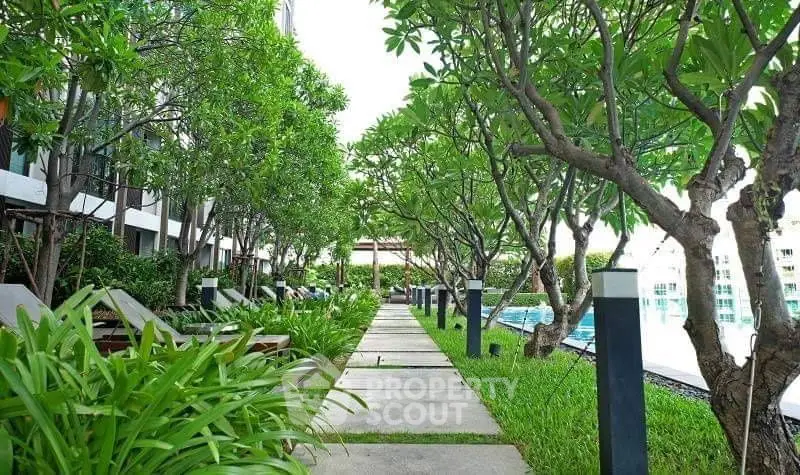 Luxurious garden pathway with lush greenery and poolside view in modern residential complex.
