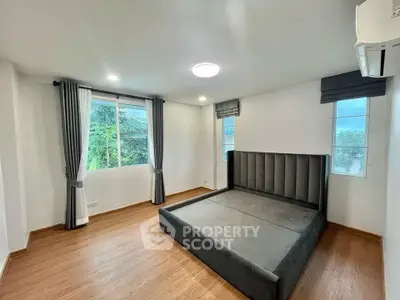 Spacious bedroom with large windows and modern bed frame, featuring elegant curtains and wooden flooring.