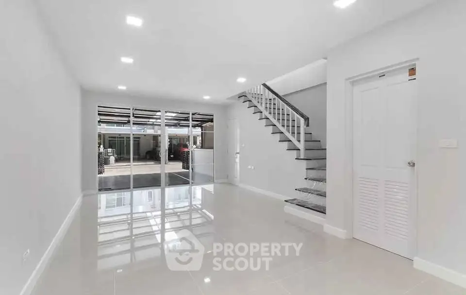 Spacious modern living room with sleek staircase and glass doors leading to outdoor area.