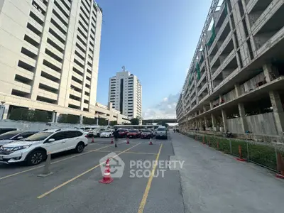 Expansive urban parking area flanked by high-rise buildings under a clear blue sky, showcasing the convenience of city living with ample parking space.