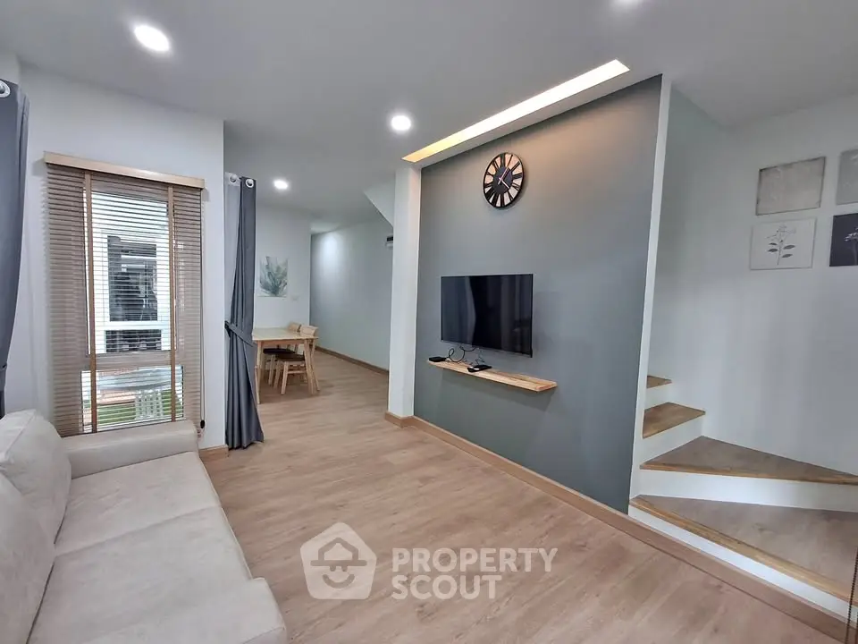 Modern living room with sleek design, featuring a wall-mounted TV and stylish staircase.