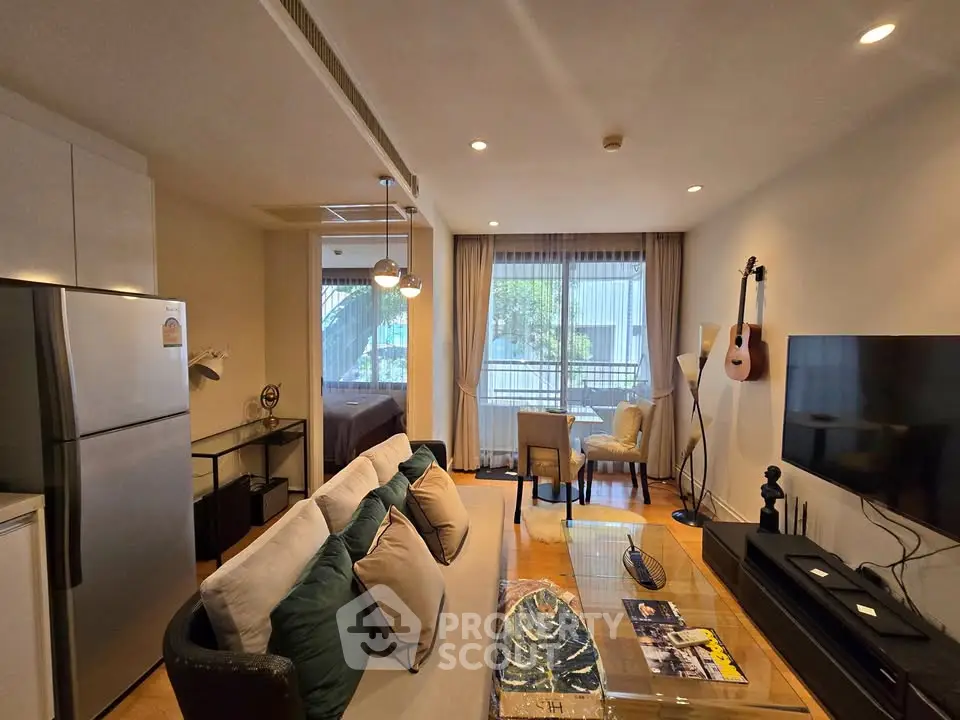 Modern living room with open layout, featuring cozy seating, wall-mounted TV, and large window for natural light.