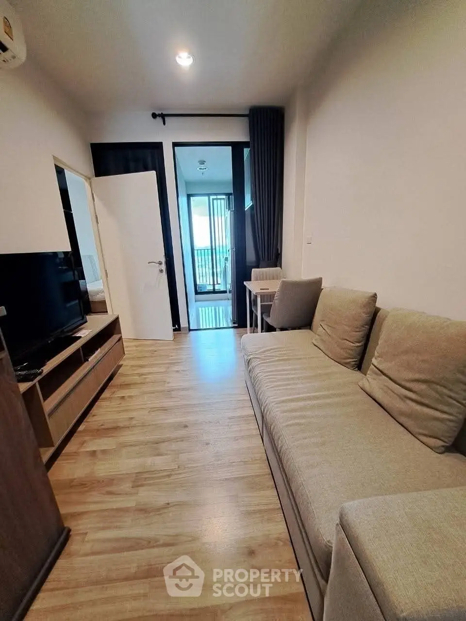 Cozy living room with modern sofa and TV unit, leading to a balcony with natural light.