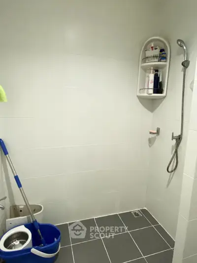 Modern bathroom with shower and cleaning supplies, featuring sleek white tiles and minimalist design.