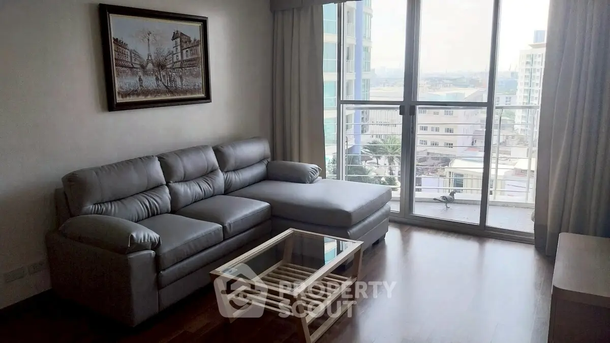 Modern living room with large window and city view, featuring a comfortable gray sofa and glass coffee table.