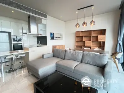 Modern living room with open kitchen, stylish gray sofa, and elegant pendant lights.