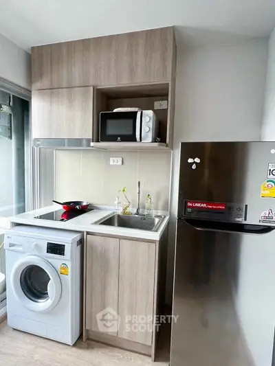 Modern compact kitchen with washing machine, microwave, and fridge in sleek apartment.