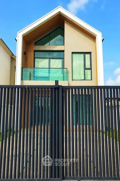 Modern two-story house with sleek design and glass balcony, featuring a stylish facade and gated entrance.
