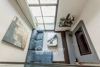 Modern living room with blue sofa and large windows, featuring stylish decor and natural light.