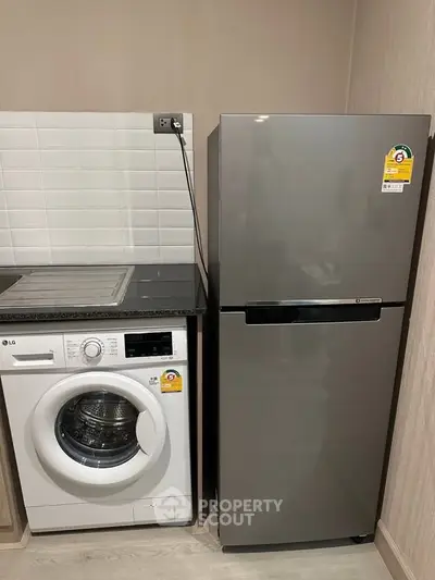 Modern kitchen with sleek fridge and washing machine in compact layout.