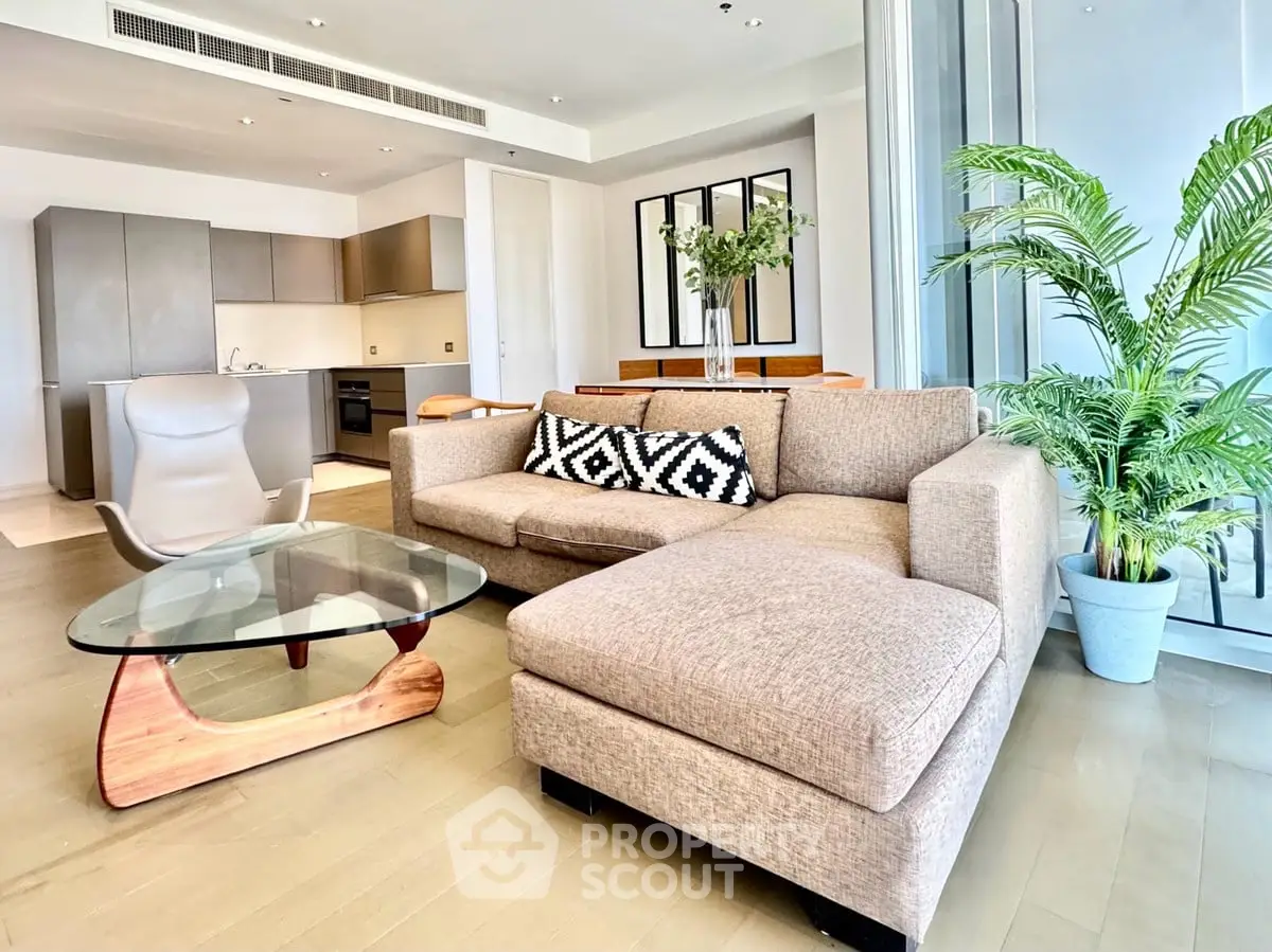 Modern living room with stylish furniture and open kitchen layout, featuring a cozy sectional sofa and glass coffee table.
