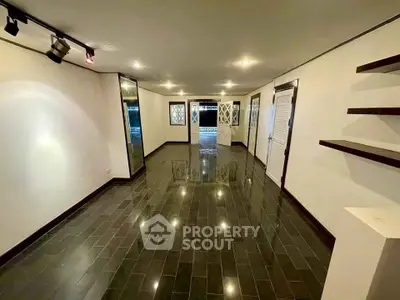 Spacious empty room with glossy dark tile flooring and modern lighting