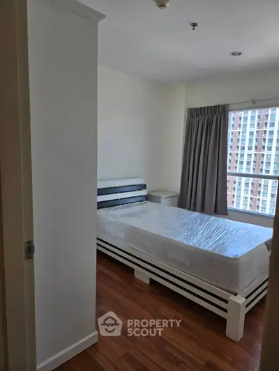 Modern bedroom with wooden flooring and large window offering city view