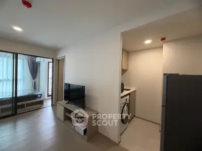 Modern apartment interior with open living room and kitchen featuring washing machine and TV setup.