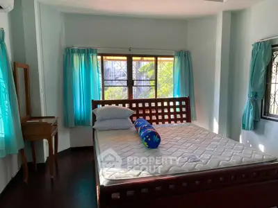 Bright bedroom with large windows and wooden furniture, featuring a comfortable bed and natural light.