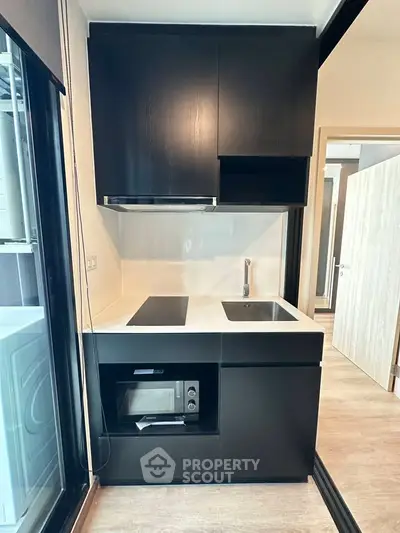 Modern compact kitchen with sleek black cabinetry and built-in appliances in a stylish apartment.
