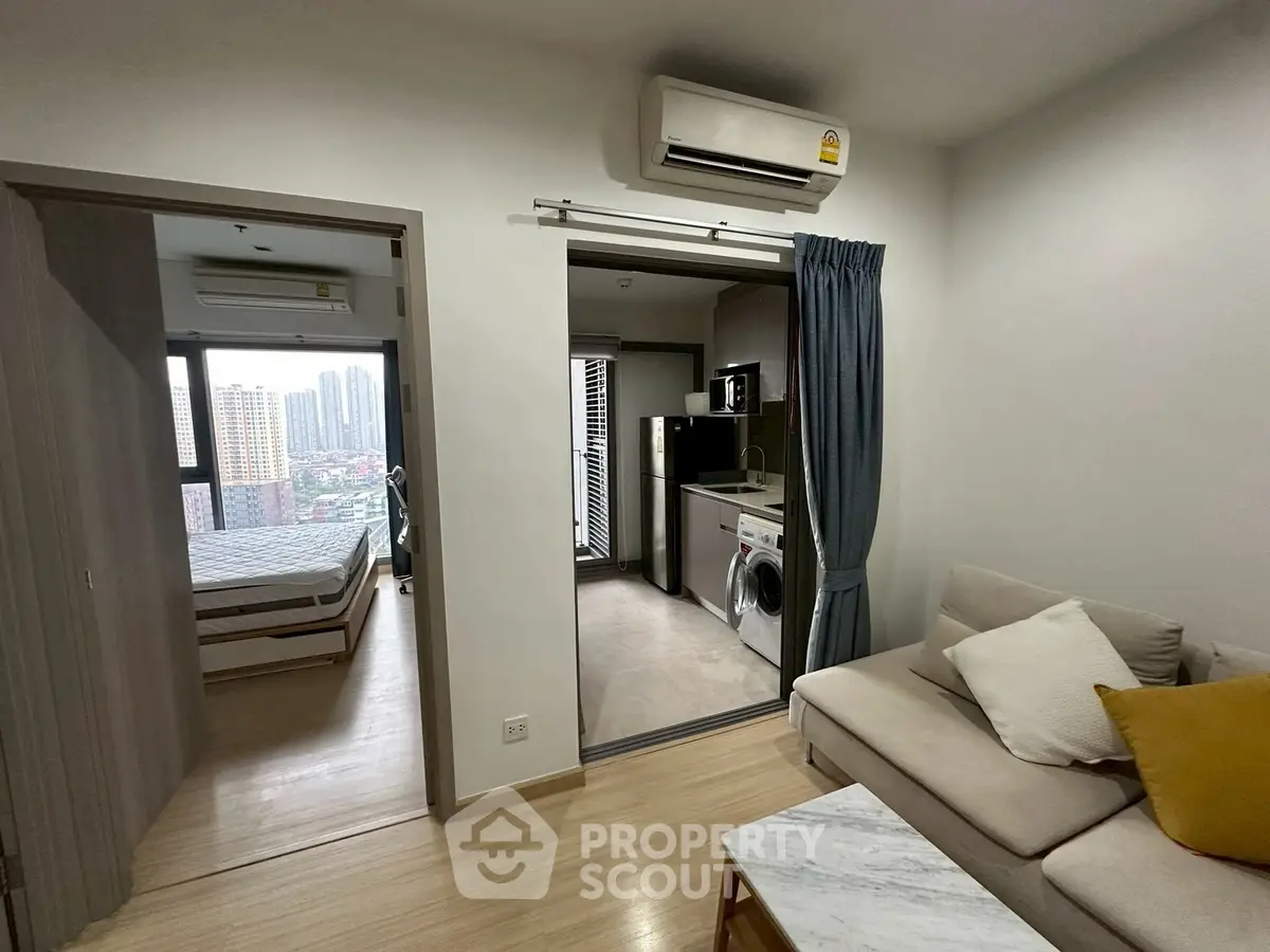 Modern apartment with open living area, bedroom, and kitchen featuring washing machine and microwave.