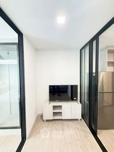 Modern apartment interior with sleek design and glass partitions, featuring a compact entertainment area.