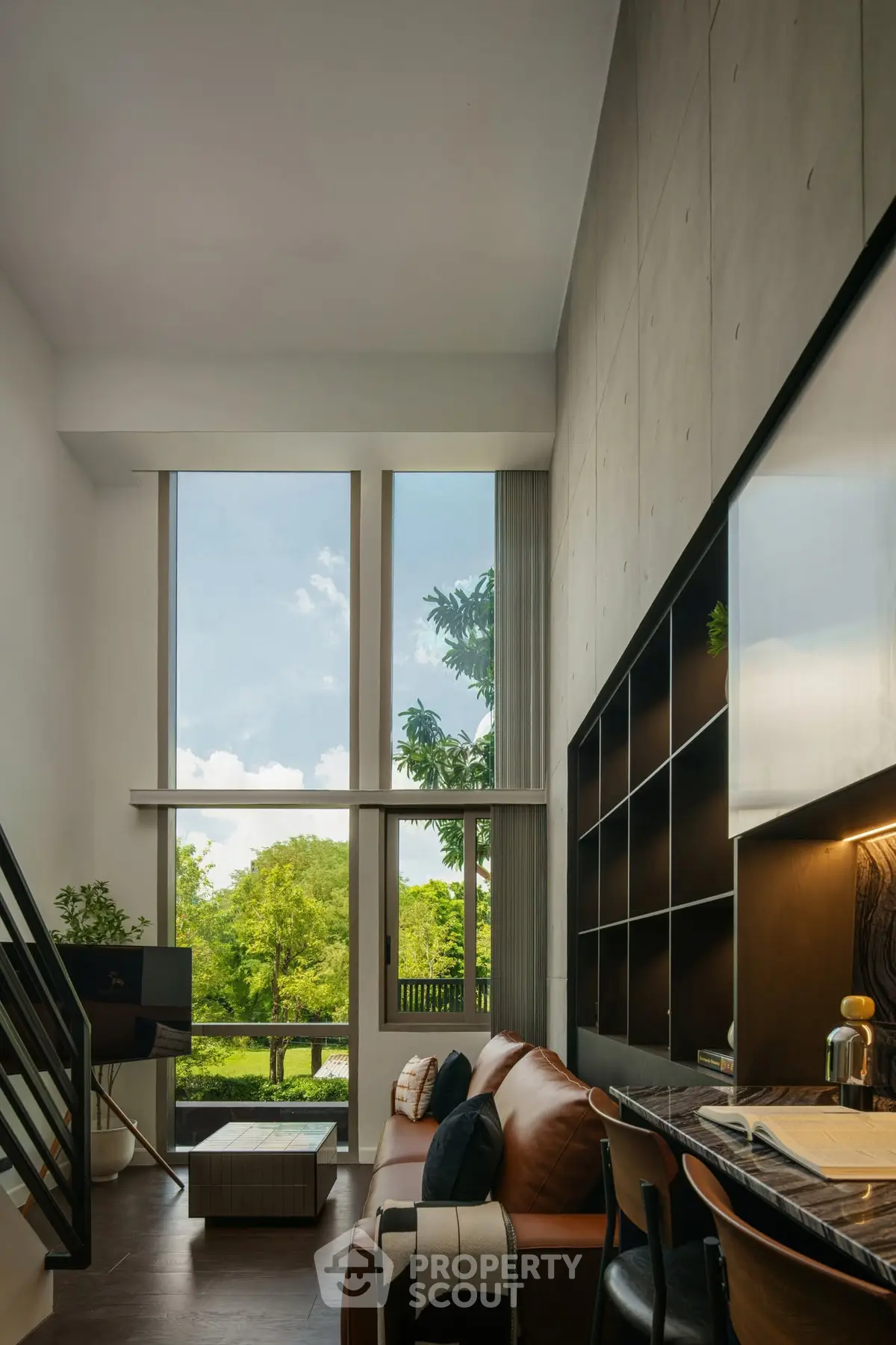 Modern living room with high ceilings and large windows offering lush green views.