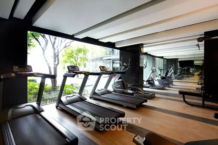 Modern gym with treadmills and large windows overlooking greenery.