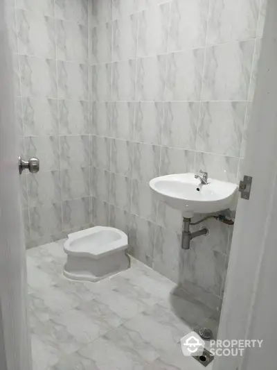 Minimalist bathroom with tiled walls and floor featuring a wall-mounted sink and squat toilet.