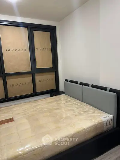 Modern bedroom with new mattress and stylish headboard, featuring large windows with privacy covers.