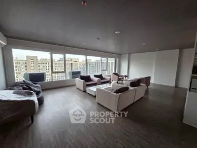 Spacious modern living room with large windows and city view, featuring elegant furniture and wooden flooring.