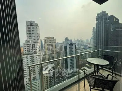 Stunning cityscape view from a high-rise balcony with modern glass railing and outdoor seating.