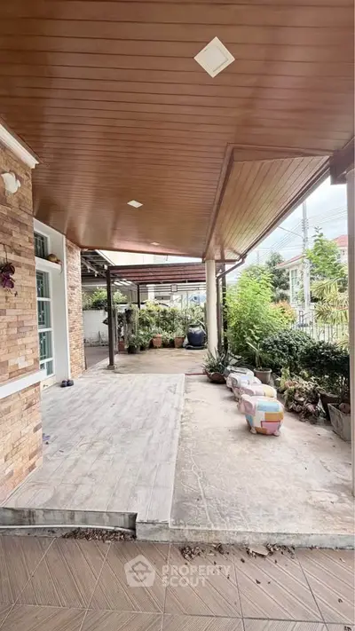 Charming covered patio with wooden ceiling and lush garden view, perfect for outdoor relaxation.
