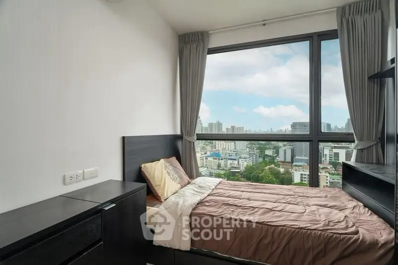 Modern bedroom with city view, featuring sleek furniture and large window for natural light.