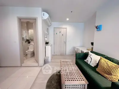 Modern living room with green sofa, stylish decor, and adjacent bathroom in a cozy apartment.