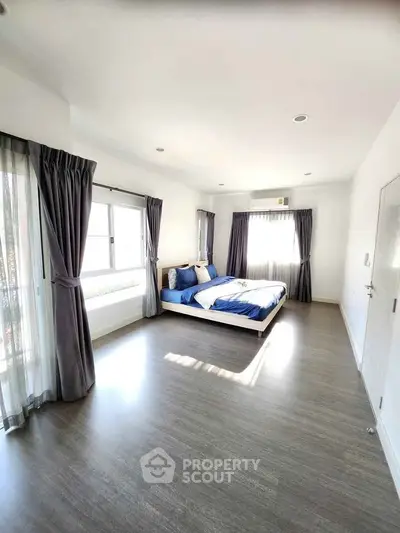 Spacious modern bedroom with large windows and elegant curtains, featuring sleek flooring and stylish decor.