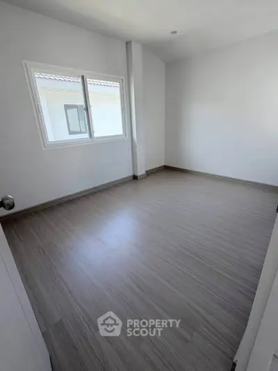 Spacious empty bedroom with large window and modern flooring, perfect for customization.