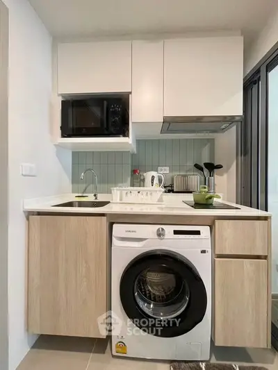 Modern compact kitchen with washing machine and microwave in stylish apartment.