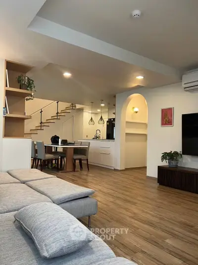 Modern open-plan living room with stylish dining area and staircase, featuring elegant decor and warm lighting.