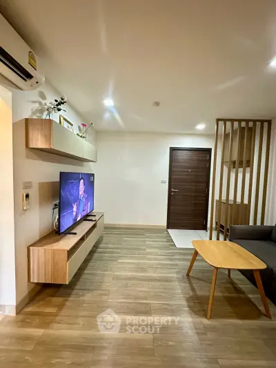 Modern living room with wooden flooring, stylish TV unit, and cozy seating area.