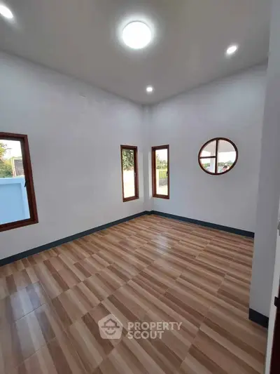 Spacious empty room with wooden flooring and round window, perfect for customization.