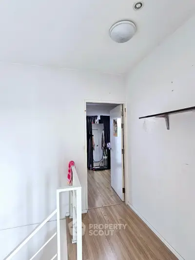 Modern hallway with wooden flooring and white walls leading to a bright room