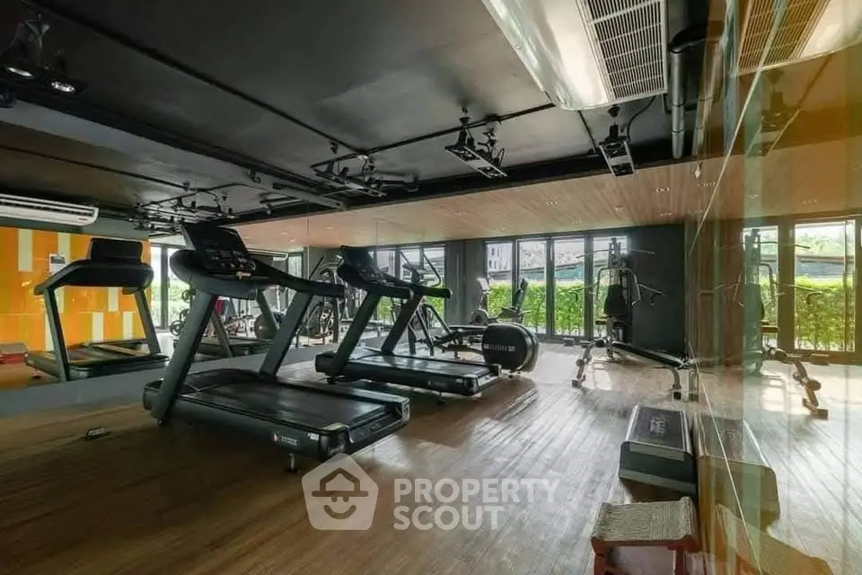 Modern gym with state-of-the-art equipment and large windows in luxury apartment complex.