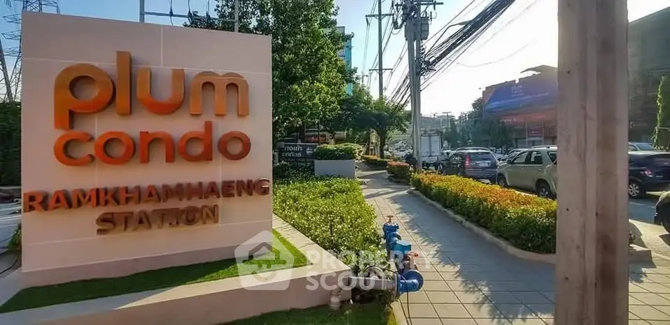 Entrance of Plum Condo Ramkhamhaeng Station with lush greenery and clear pathway.
