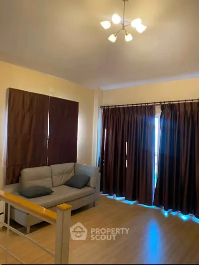 Cozy living room with modern lighting and large windows with brown curtains.