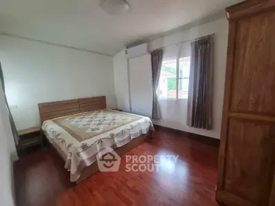 Spacious bedroom with wooden flooring and large window for natural light.