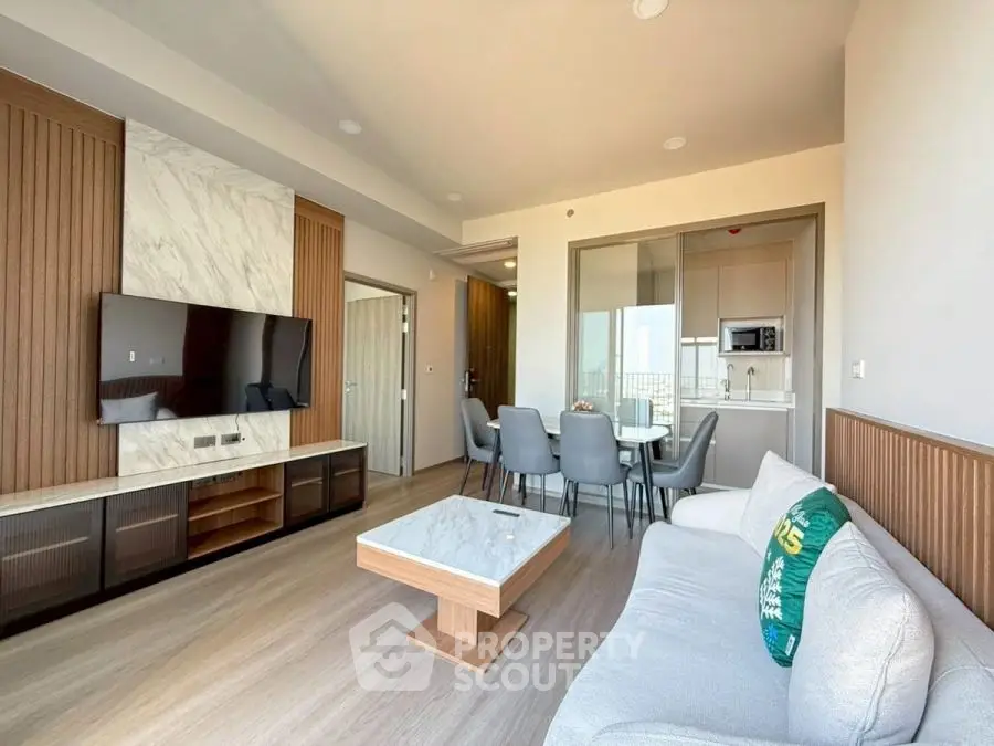 Modern living room with elegant decor and open dining area, featuring a sleek TV setup and stylish furniture.