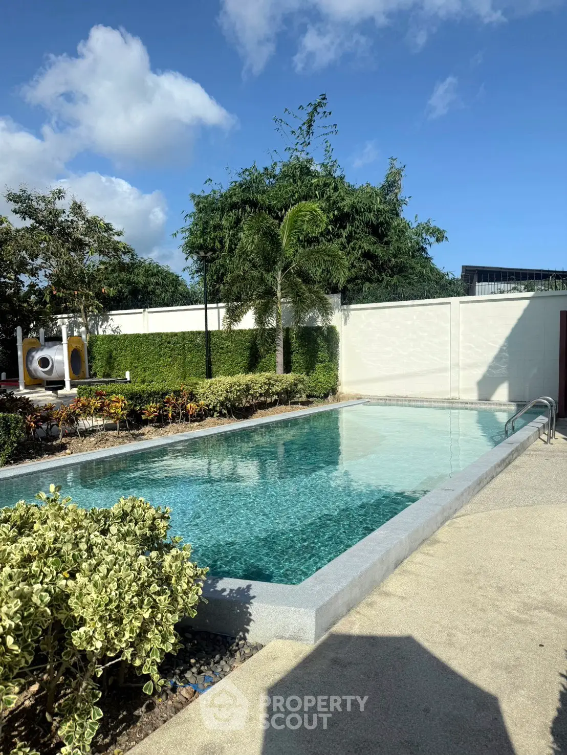 Luxurious outdoor pool area with lush greenery and clear blue skies, perfect for relaxation and leisure.
