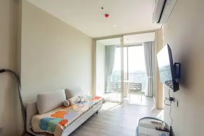 Bright modern living room with large windows and balcony, featuring cozy sofa and wall-mounted TV.