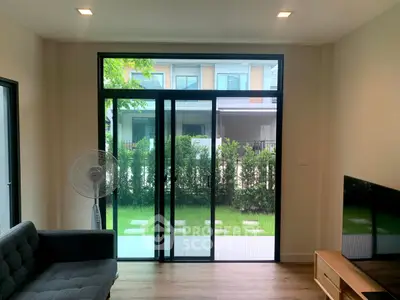 Modern living room with large glass doors opening to a lush garden view, featuring sleek furniture.