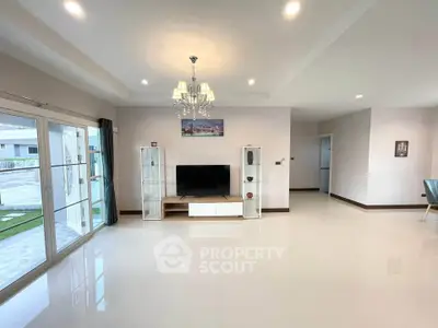 Spacious modern living room with elegant chandelier and large windows offering natural light.