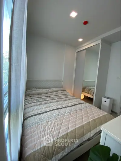 Cozy bedroom with modern decor and ample natural light from large window.