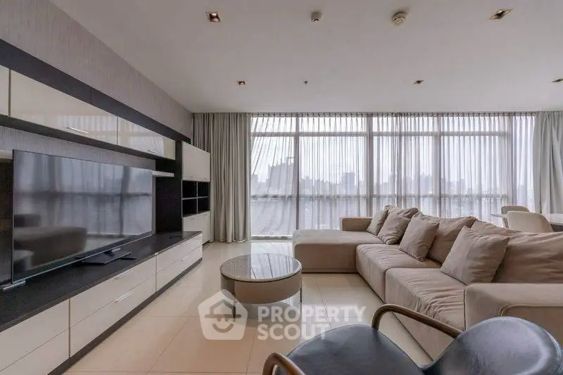 Spacious modern living room with large windows and city view, featuring a sleek entertainment unit and comfortable seating.
