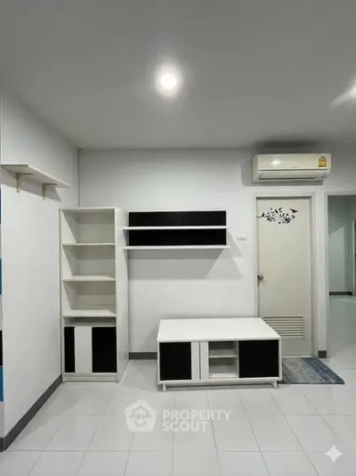 Modern minimalist living room with sleek white and black furniture, featuring built-in shelves and air conditioning.